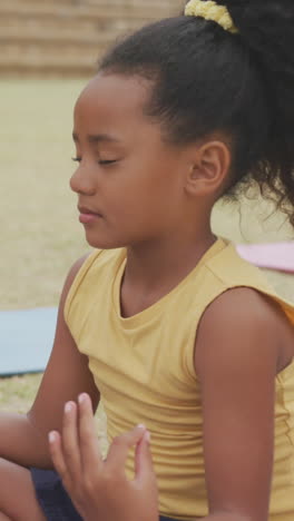 video of focused diverse girls practicing yoga on mats in front of school