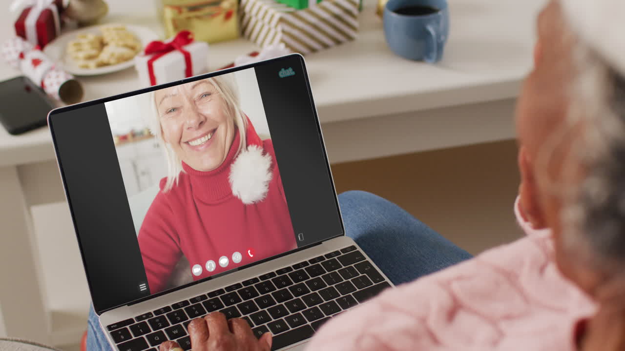 mujer afroamericana con sombrero de santa teniendo llamada de video portátil con mujer caucásica feliz