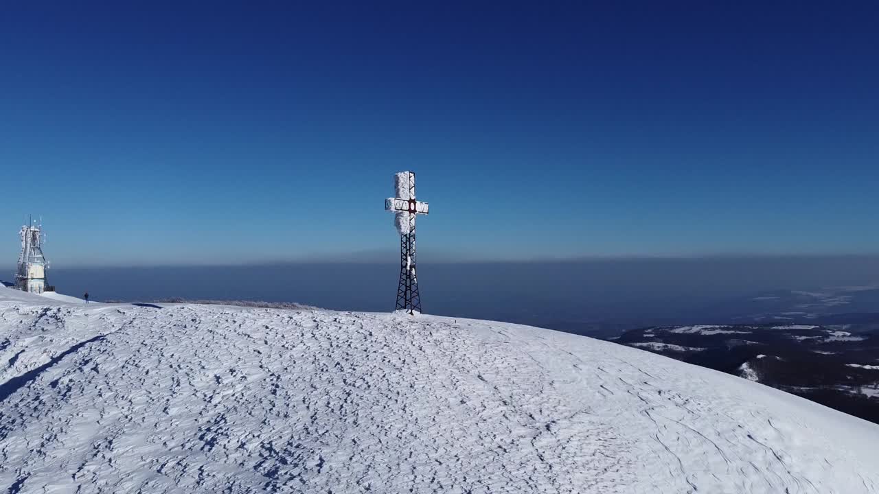 Aerial alpine peak with cross on top of scenic mountains crest, drone reveals stunning natural winter snow covered landscape in remote unpolluted natural environment