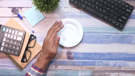 persona con las manos en la taza de café y el plato en el escritorio de trabajo