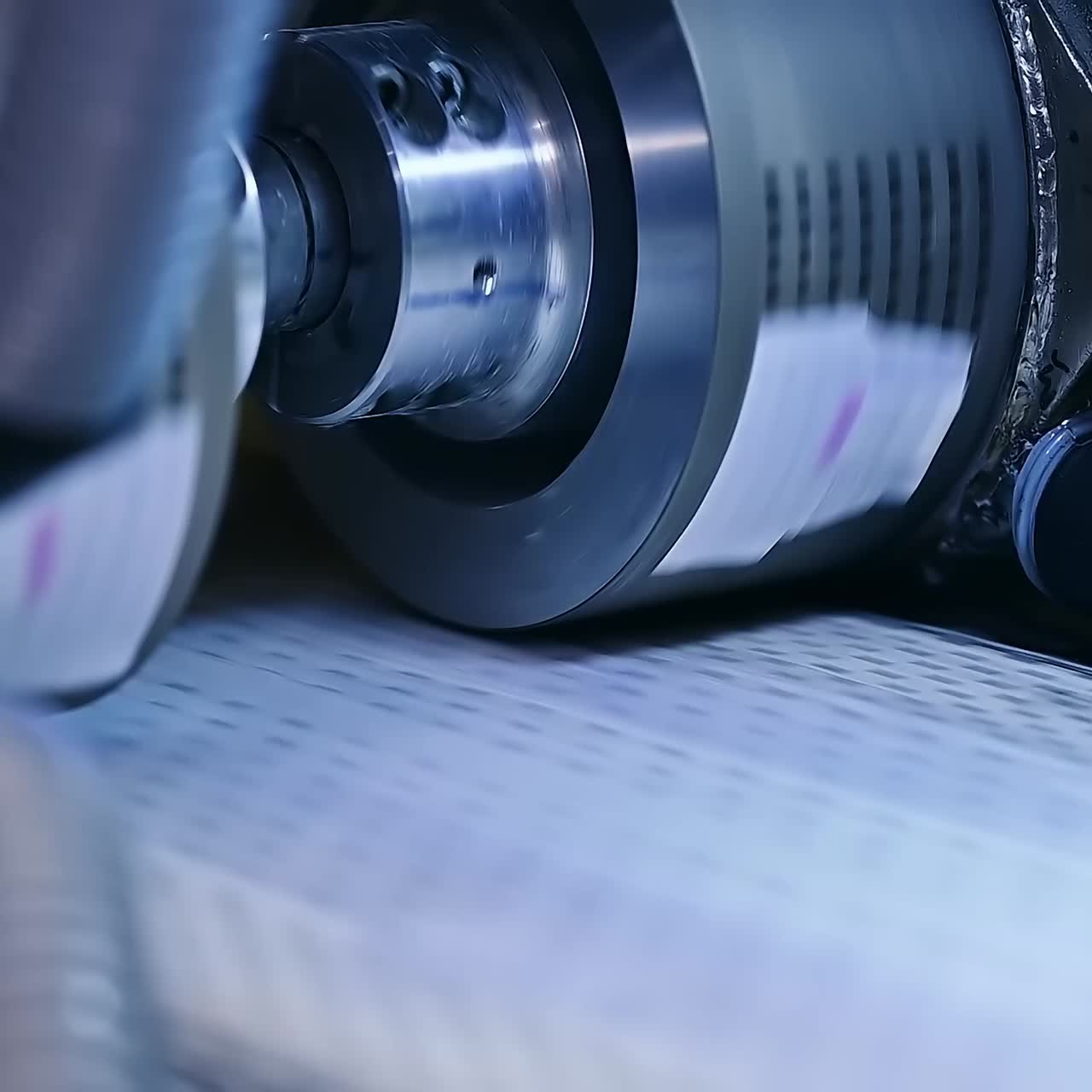 Conveyor line with special material for nappies manufacturing. Rotating rollers over the line of conveyor. Close up