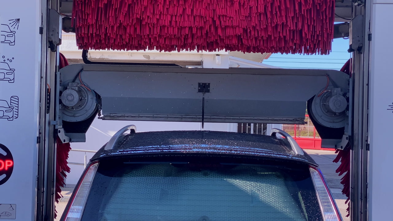 Car undergoing an automated washing process with rotating brushes and water in a modern commercial car wash facility