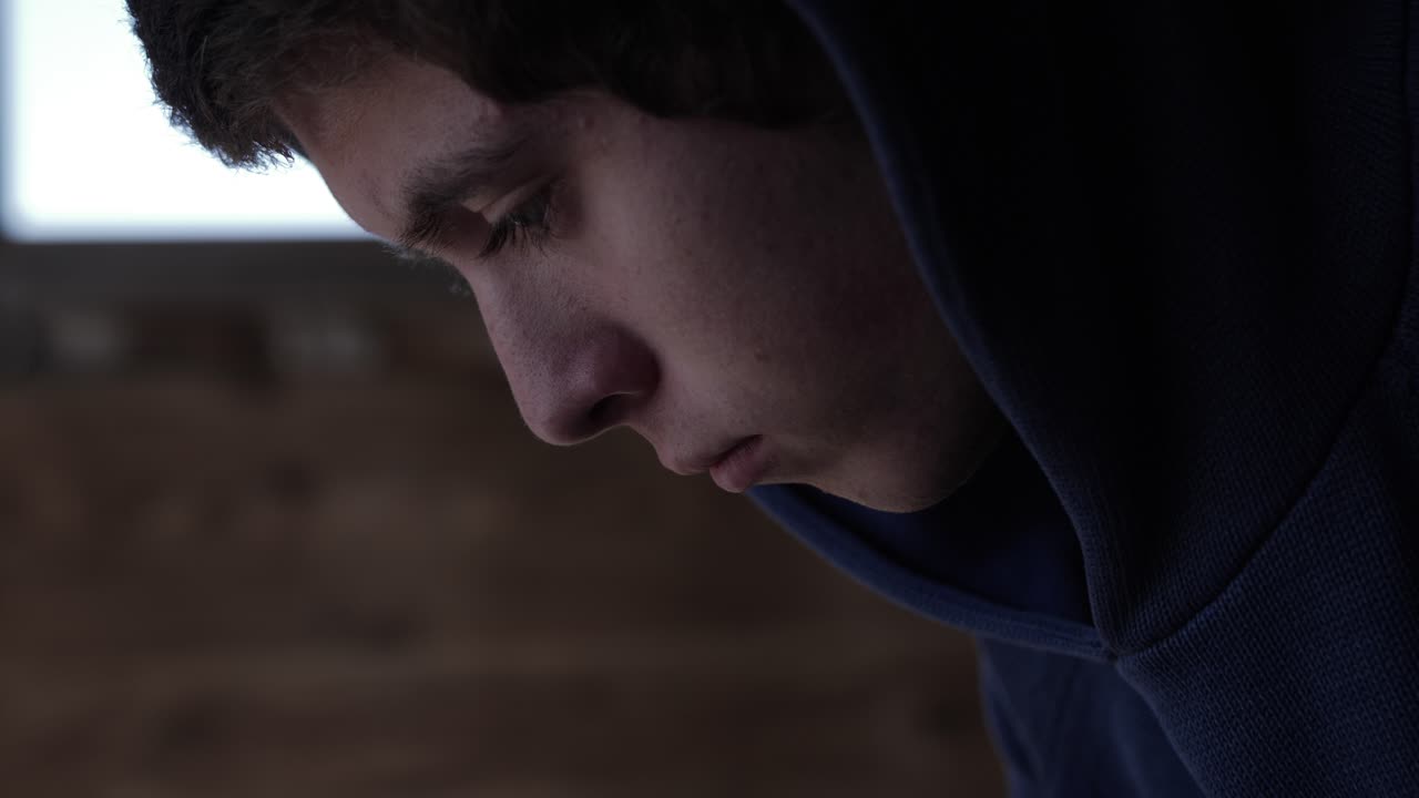 Um close-up, de perfil, de um jovem adolescente com semblante triste.