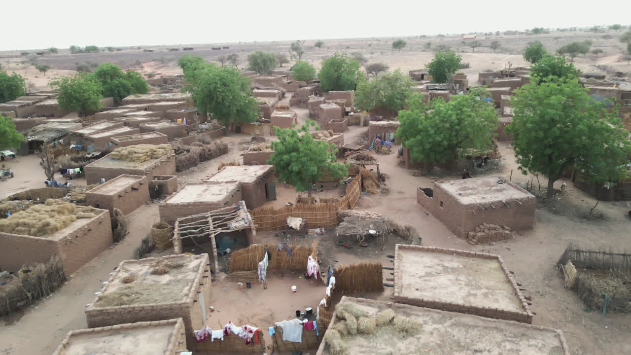 Drone spirals sideways over a rural village with earthen homes in Nigeria during daytime, capturing daily life and unique architecture from above