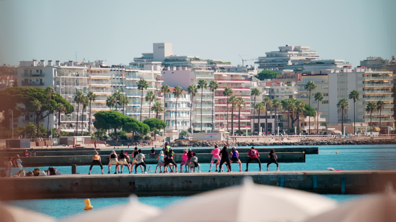Cannes, France - October 7, 2025: A group of people practicing dance or fitness on a pier by the sea on a sunny day