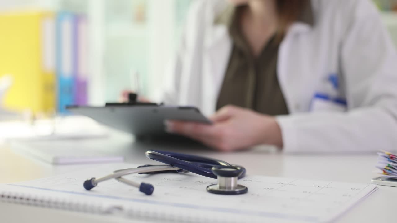 A doctor working at a desk with a stethoscope in the foreground