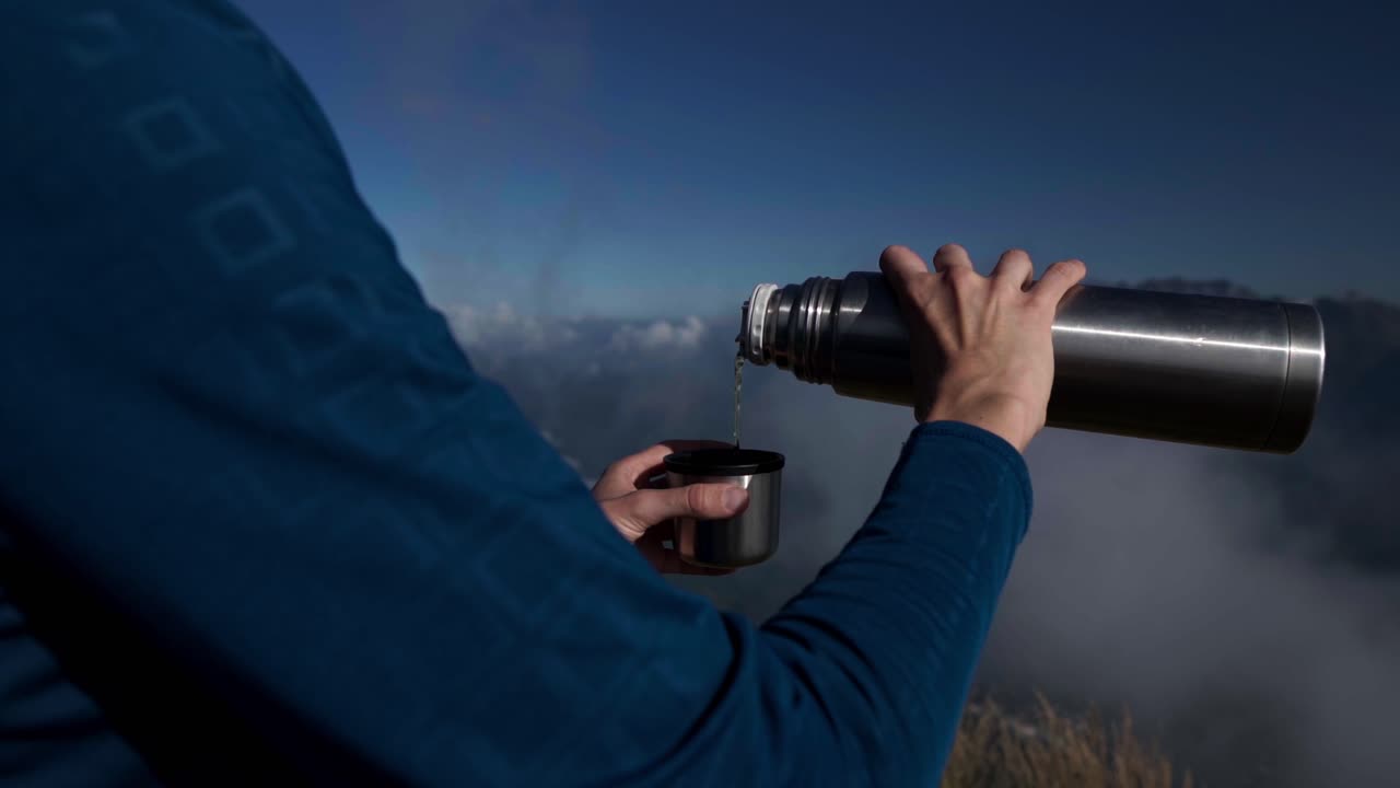 Donna che versa una bevanda calda da un thermos in cima a una montagna