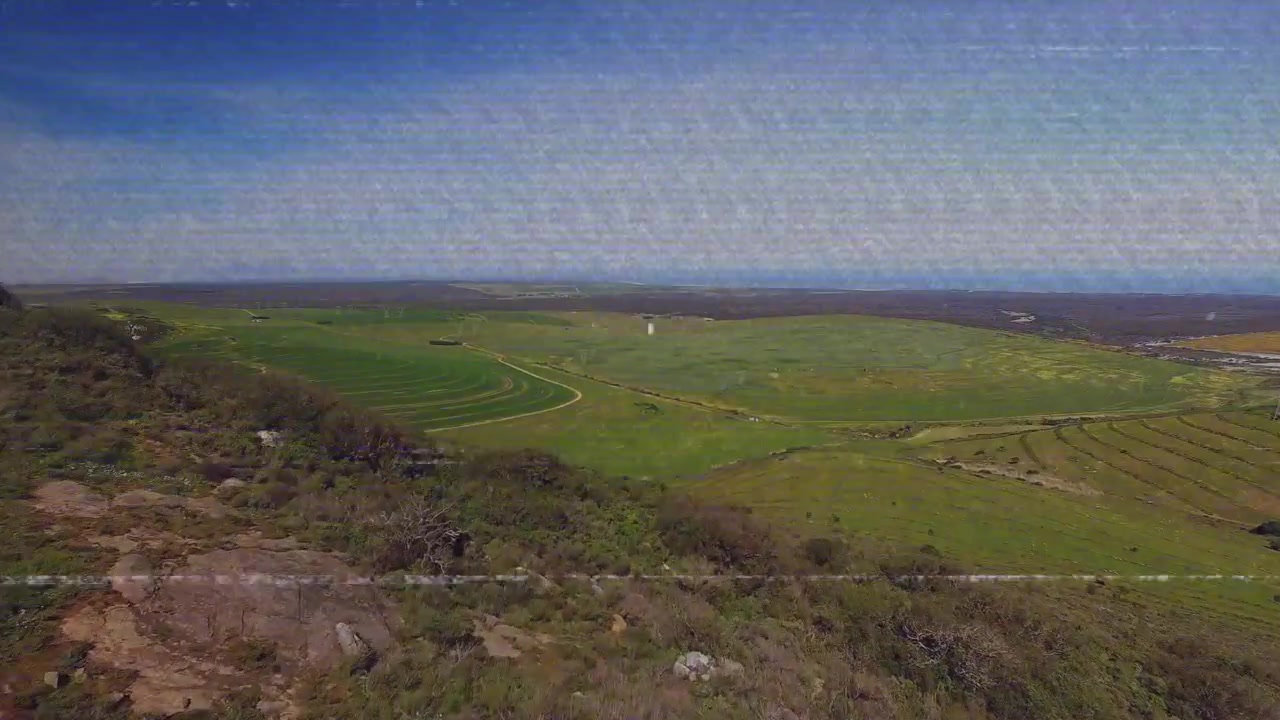 On play camera ascending hillside and panning right pulling back showing farmland and sea horizon