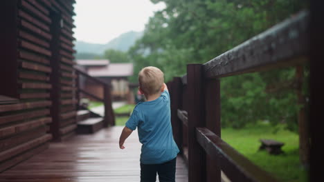 Toddler-boy-walks-touching-wooden-railing-on-veranda