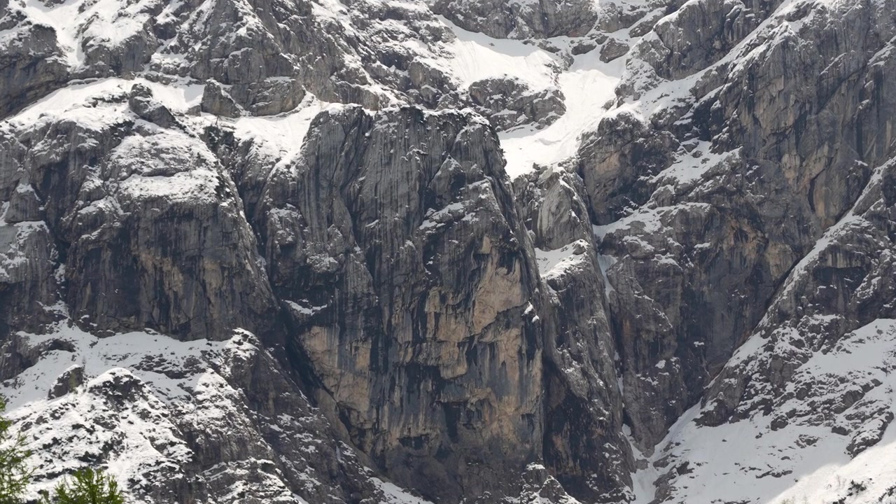 Face rochosa acidentada conhecida como Donzela Pagã (Ajdovska Deklica) na Montanha Prisank, perto do Passo Vršič, Eslovênia, cercada por neve e terreno alpino acidentado, vista aérea cinematográfica.