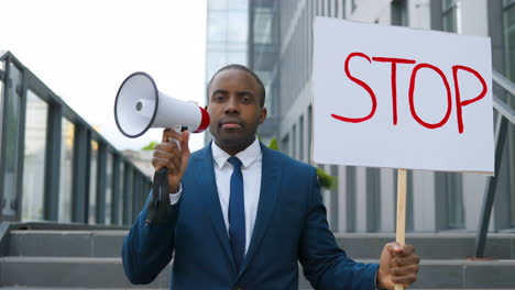 close-up view of african american elegant young man talking on a loudspeaker and holding a stop" signboard in the street"