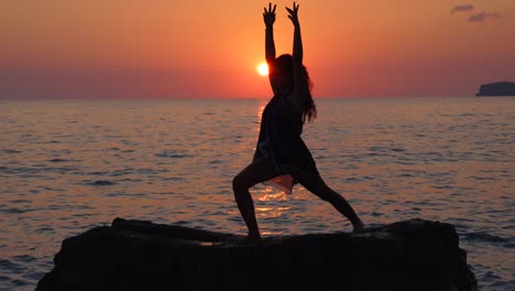 girl poses over cliff surrounded by vibrant sea water at beautiful sunset, doing yoga exercises