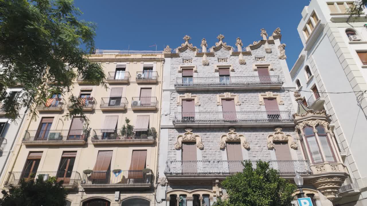 Low angle view of residential buildings with ornate stone facades and balconies, showcasing modernist architecture in Tarragona, Spain