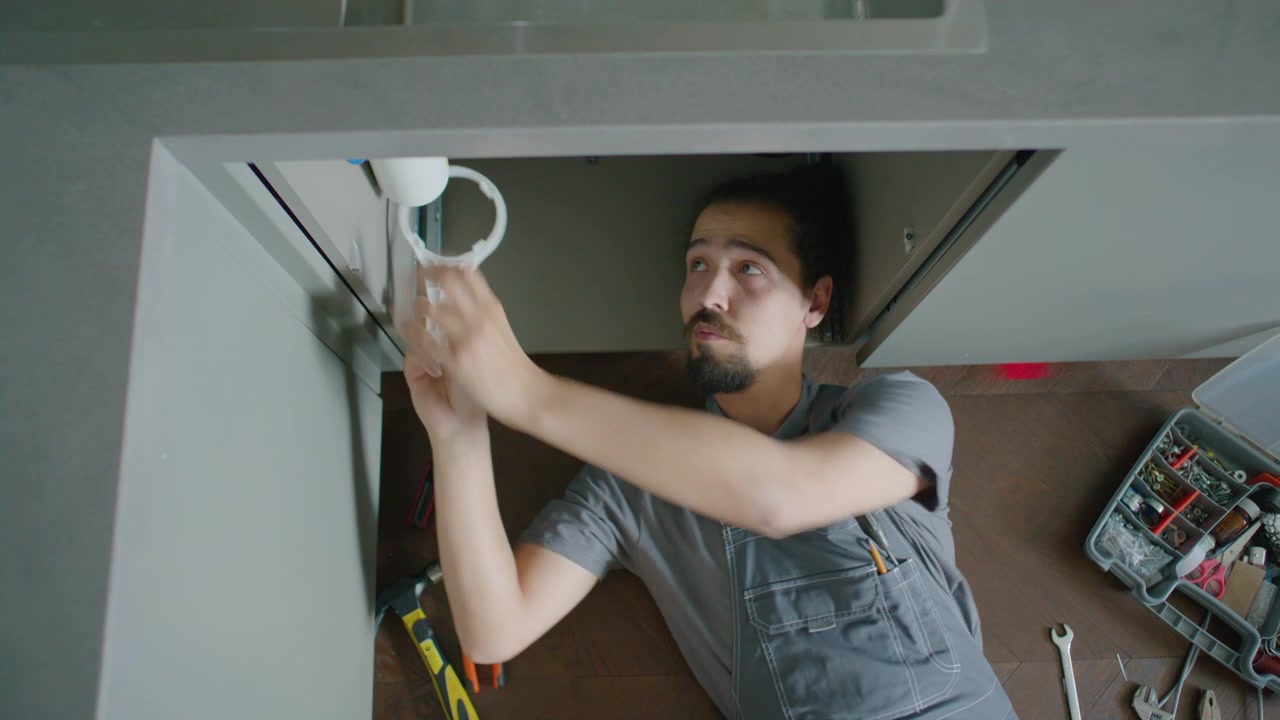 Top Down of Handyman Lying on Floor, Repairing Kitchen Plumbing