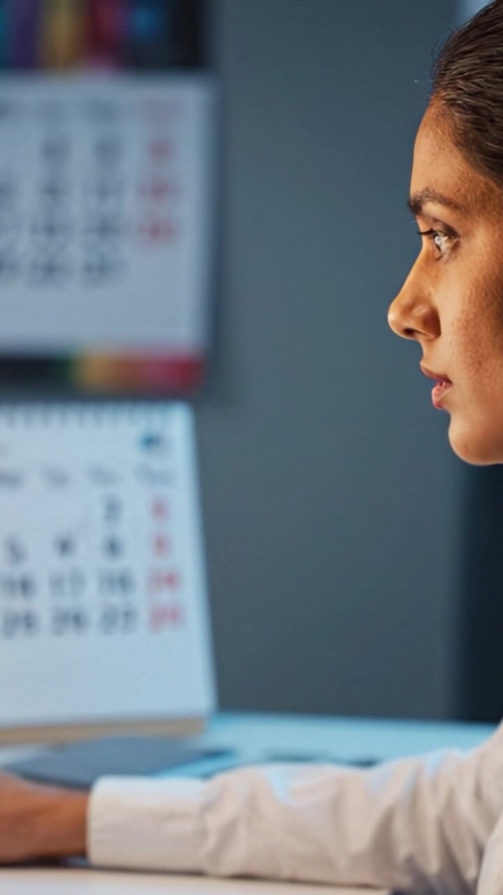 Donna professionista concentrata che riflette sui compiti mentre guarda un calendario durante una sessione serale, con una luce soffusa che crea un'atmosfera ispiratrice.