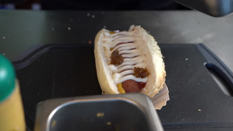 close-up view of putting bacon bits on top of mayonnaise on a hotdog sandwich