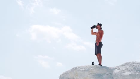 an athletic man drinks an energy drink from a bottle after training outdoors. slow motion
