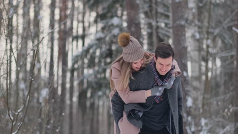 Ein-Junger-Mann-Und-Eine-Frau-Im-Mantel-Amüsieren-Sich-Und-Spielen-In-Zeitlupe-Mit-Schnee-In-Einem-Winterwald.-Glück-Und-Lächeln-Auf-Den-Gesichtern