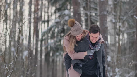 a young man and a woman in a coat are having fun and playing with snow in a winter forest in slow motion. happiness and smiles on faces