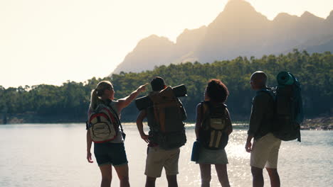 rear view group of friends with backpacks on vacation hiking looking at lake and mountains