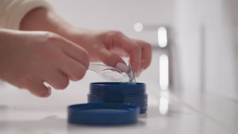 hand of woman takes patch for skin of eyes using cosmetic spatula. lady with manicure takes cosmetic eye patches from jar in bathroom slow motion