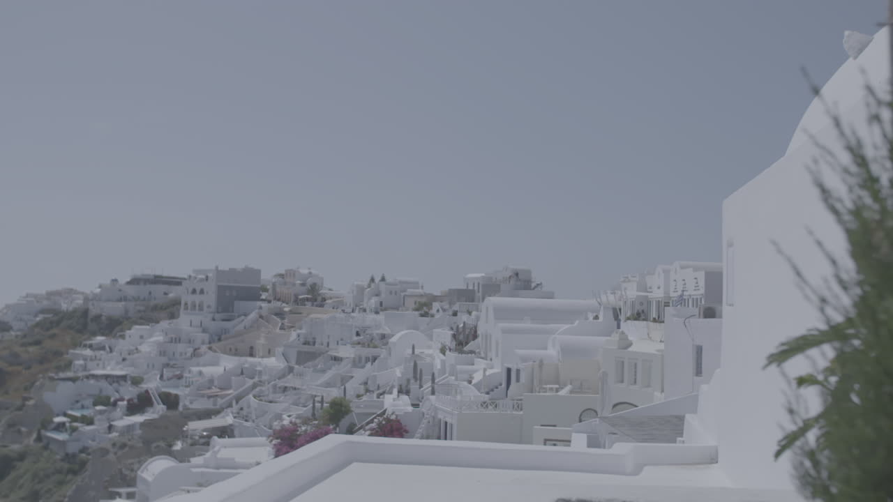 Overview of Santorini Greece on a sunny day seen from a terrace with plants in front in slowmotion and the sea in the background reflecting the sun LOG