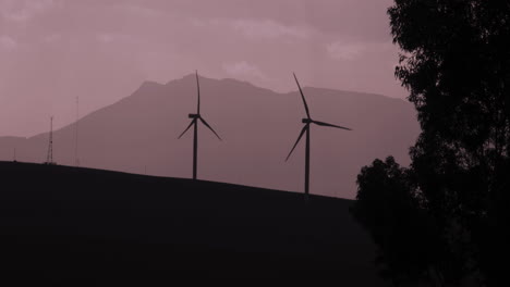 Silhouette-Drehende-Windkraftanlagen-Vor-Einem-Bewölkten-Und-Stimmungsvollen-Himmel