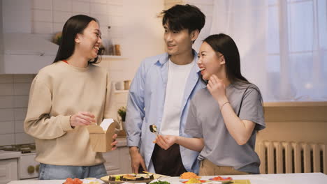 three japanese friends eating japanse food around the kitchen counter, then they look at camera, smile and doing ok sign