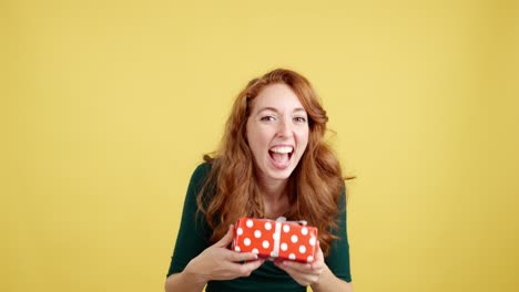 happy redhead woman showing excitement and holding a gift box on yellow background