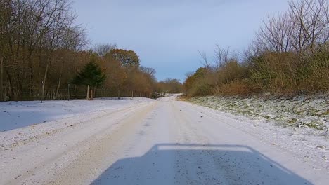 pov through the rear window while driving on a rural snowy road past timbers and farm houses on an early winter afternoon