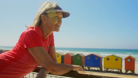 vista lateral de una mujer caucásica senior activa de pie en un paseo marítimo en la playa 4k