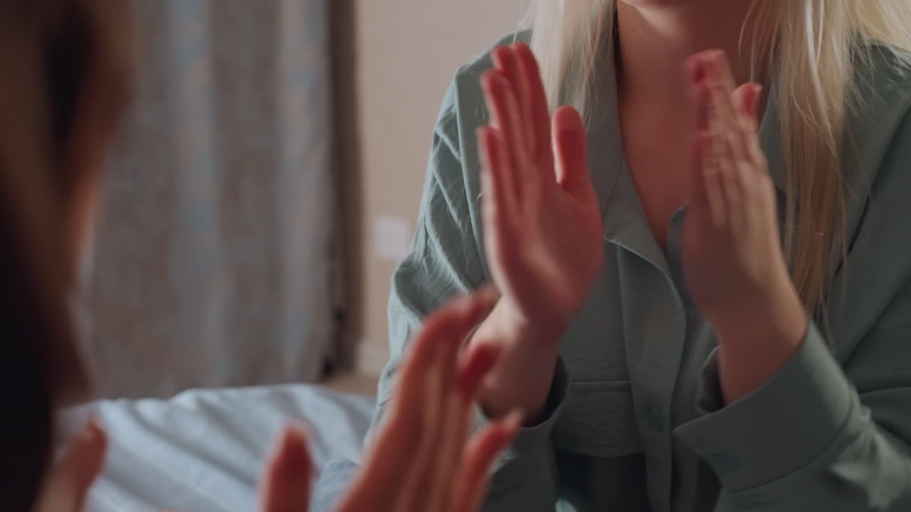 Close up of child wearing dark pajamas clapping hands playfully with unseen partner during relaxed indoor bonding moment, showing joyful energy and connection in cozy bedroom setting