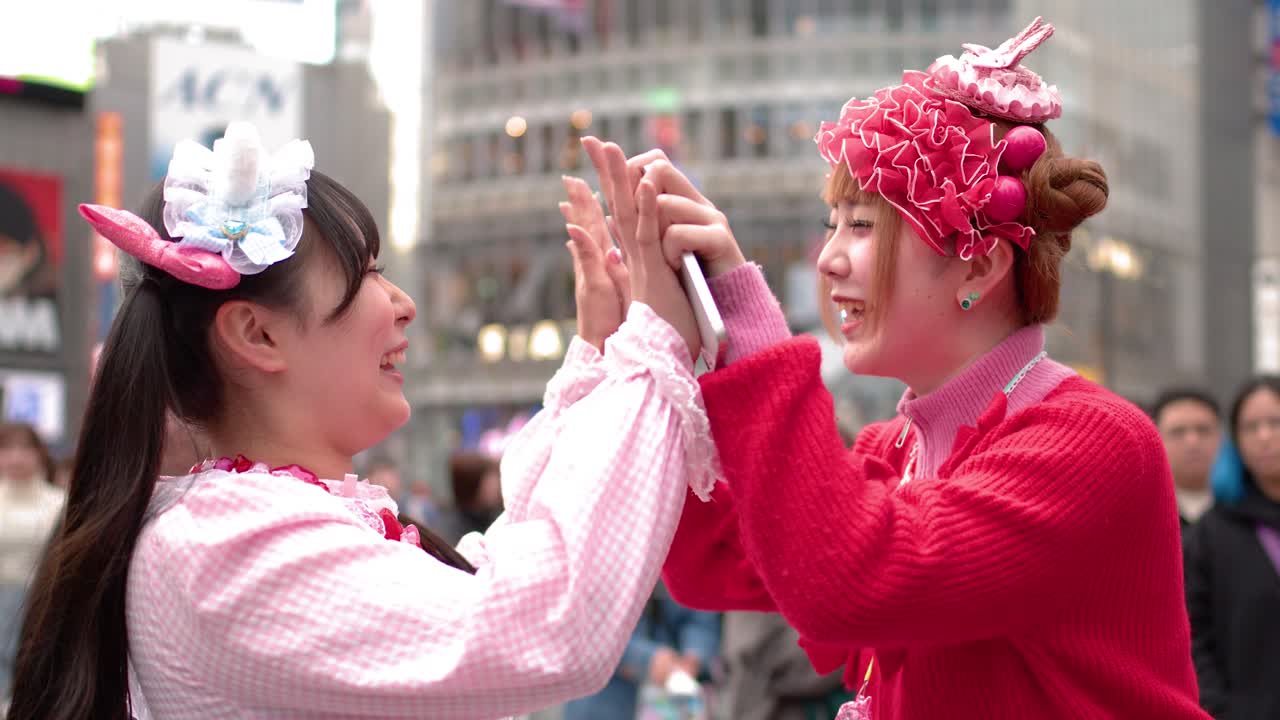 To venner i farverigt decora-mode griner og giver high five ved Shibuya Crossing i Tokyo.