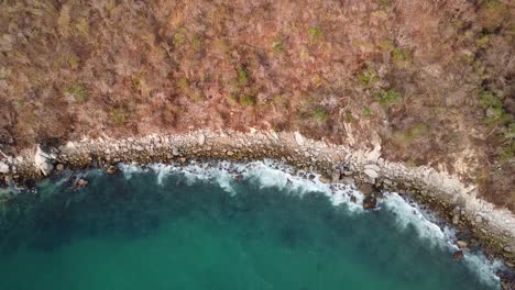 Toma-Aérea-De-Arriba-Hacia-Abajo-Que-Muestra-Olas-Del-Océano-Pacífico-Alcanzando-La-Costa-Rocosa-En-Huatulco,-México