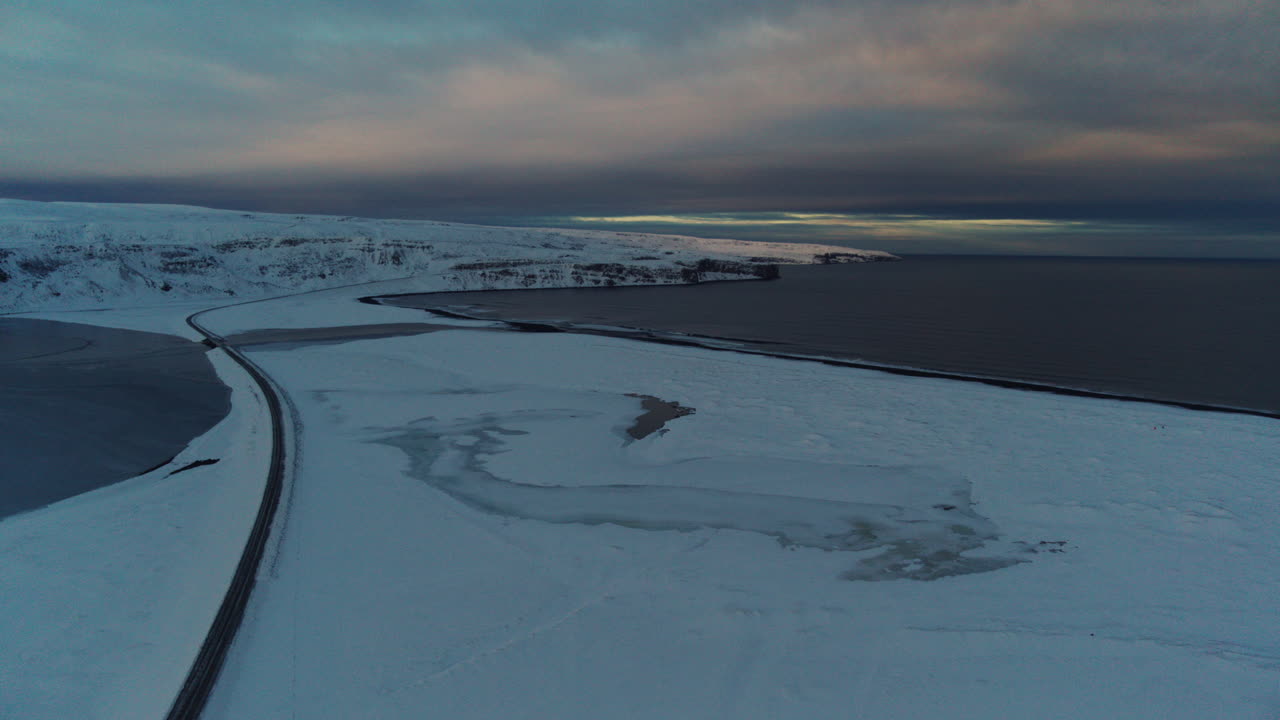 Arctic road surrounded by snowy fields under the dim winter light in Iceland, aerial pullback overview