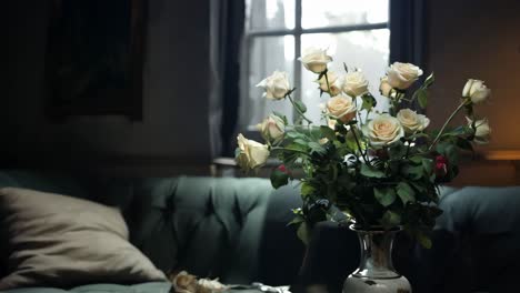 white roses arranged in a vintage vase sit on a table in a dimly lit room, with sunlight streaming through a nearby window, creating a soft and inviting atmosphere