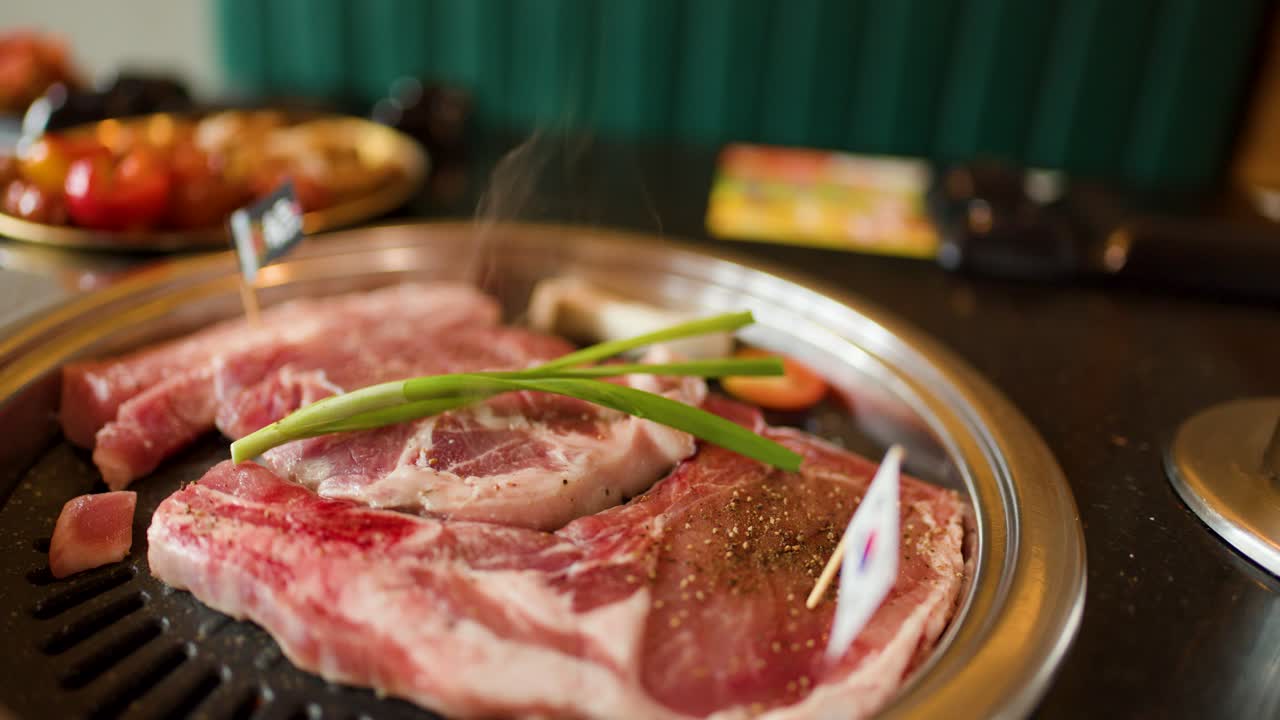Raw beef and fresh vegetables sizzling on a tabletop grill, steam rising in shallow focus