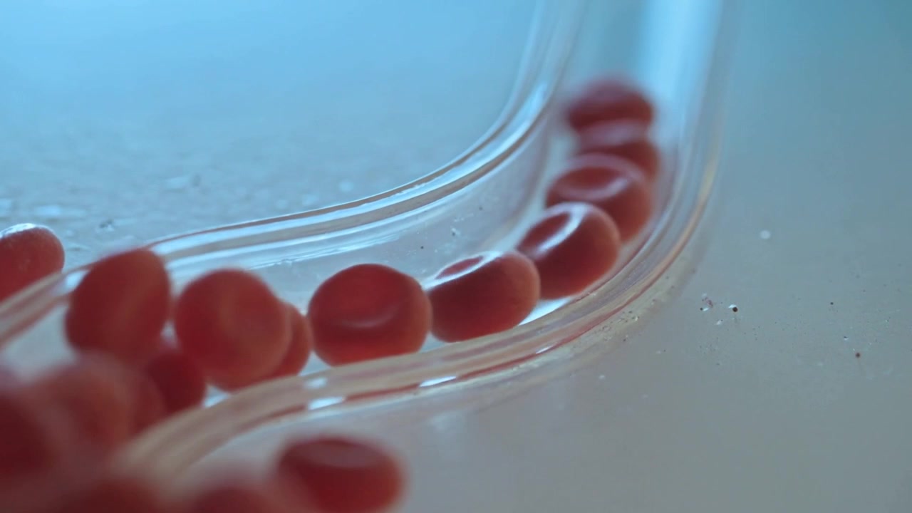 Nudging red donut bead cluster rolling, colliding, lining up along clear channel on pale tabletop