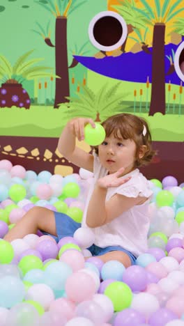 joyful little girl playing in a colorful ball pit at an indoor playground, surrounded by pastel-colored balls and a vibrant mural