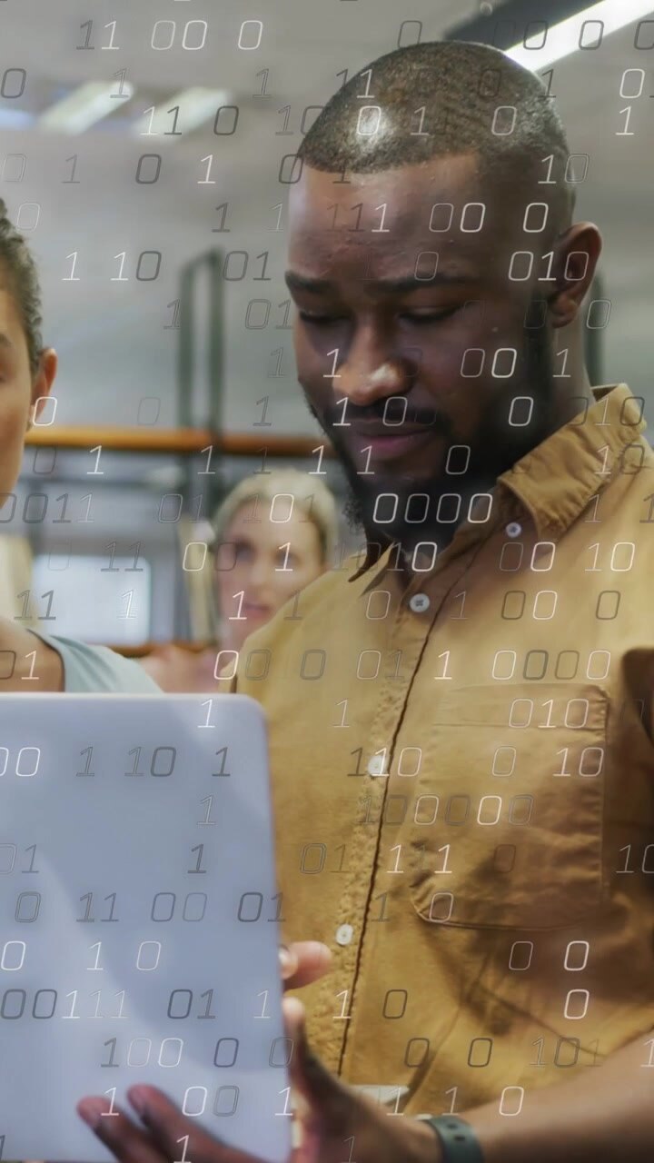 Vertical video: Man tapping white laptop, binary overlay densifying as team reviewing business data