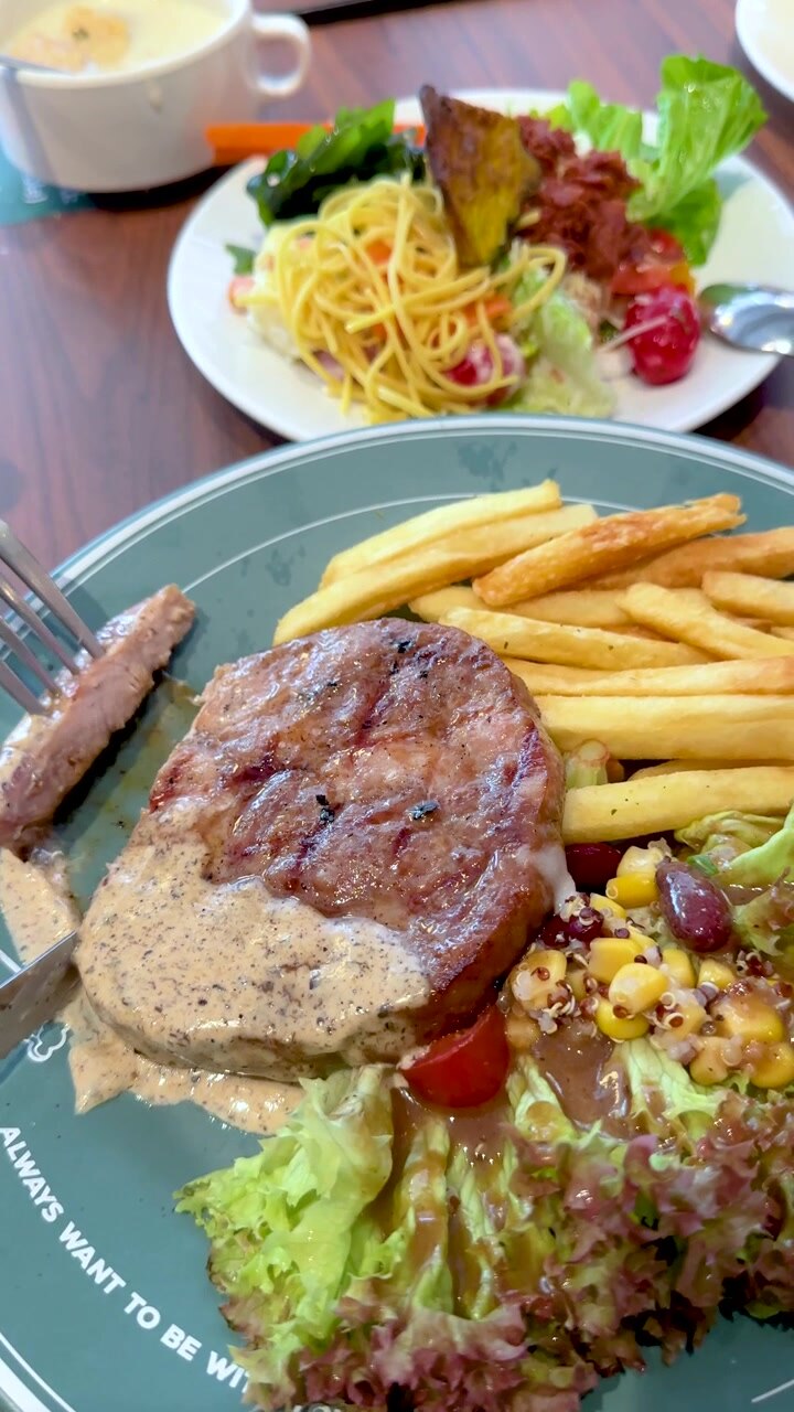 Una persona corta un bistec de cerdo a la parrilla servido con patatas fritas y ensalada en Bangkok.