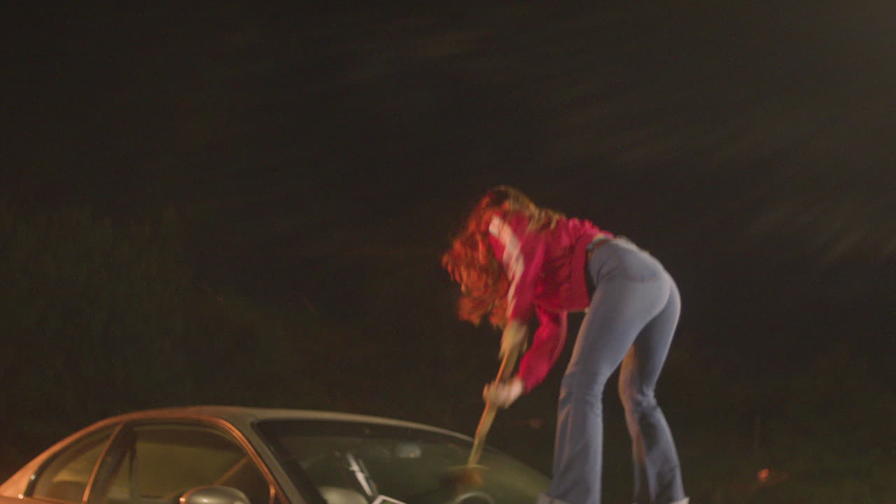 빨간 머리 여자가 자동차 앞 유리에 피자 패들을 부수다