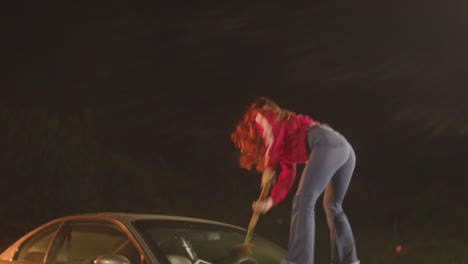 a red-haired woman smashes a pizza paddle on a car windshield