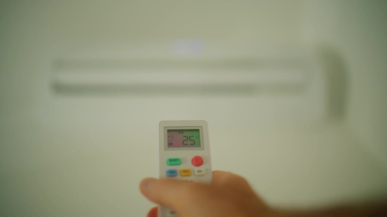 Hand holding a remote control, adjusting temperature and fan settings for an indoor air conditioner
