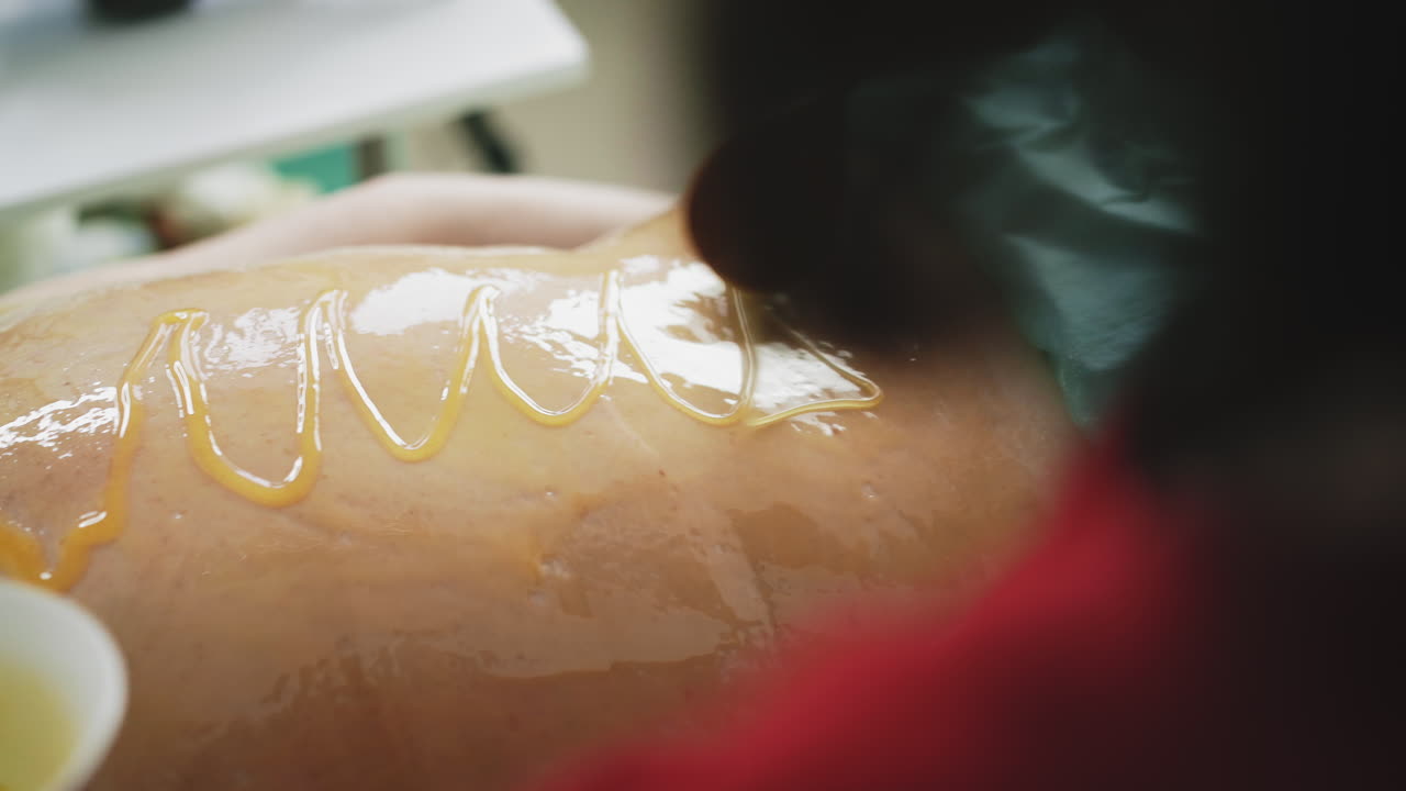 il terapeuta versa miele liquido sulla schiena del cliente, fa un massaggio.