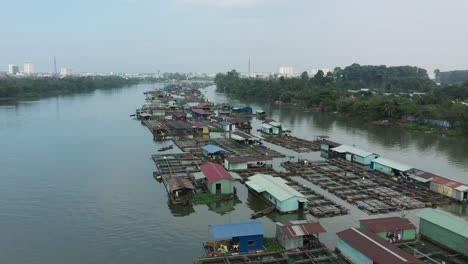 slow tracking drone shot over floating fish farming community in bien hoa on the dong nai river, vietnam on a sunny day