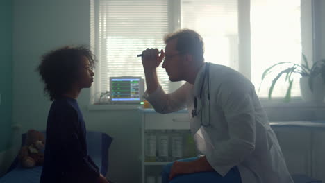 physician testing pupil reflex shining flashlight in african american girl eyes.