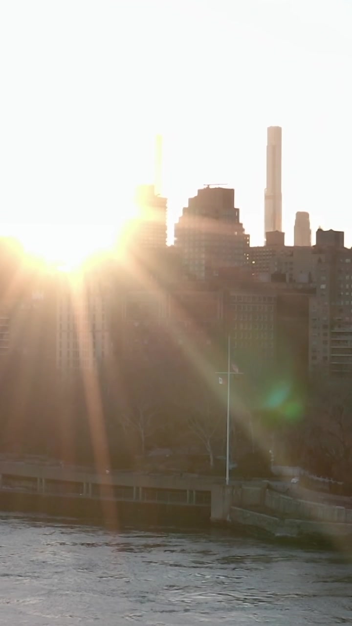 Nascer do sol sobre Nova Iorque iluminando edifícios e a água.