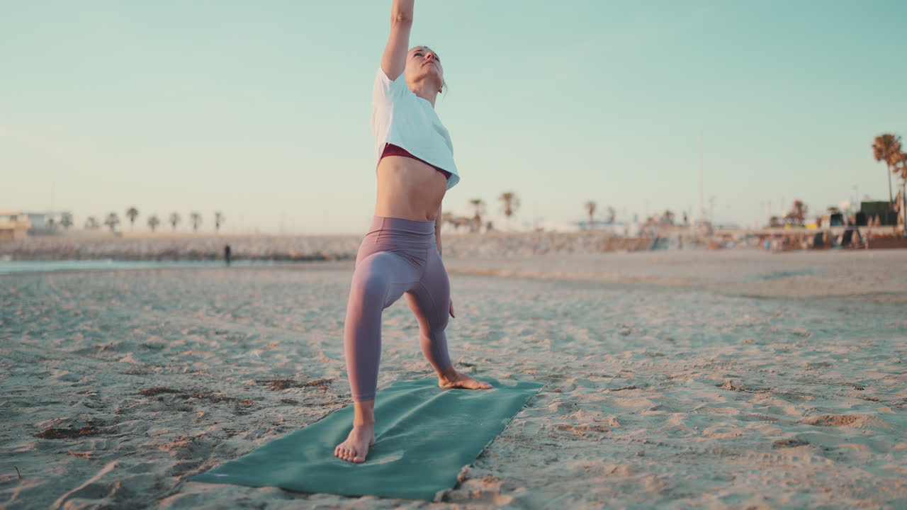 tomada completa de una chica caucásica haciendo yoga en una alfombra de fitness en la playa.