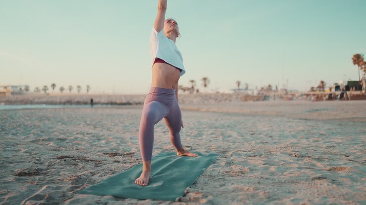 Full length shot of Caucasian girl doing yoga on fitness mat on the beach.